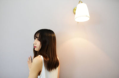 Young woman looking away while standing against white wall