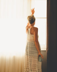Adult woman looking out of the window. view from the back with cup in her hand.