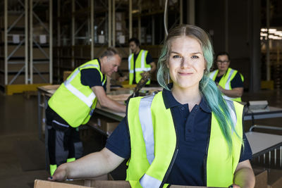 Portrait of smiling female worker with dyed hair standing against coworkers in distribution warehouse