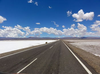 Empty road by salt flat against sky