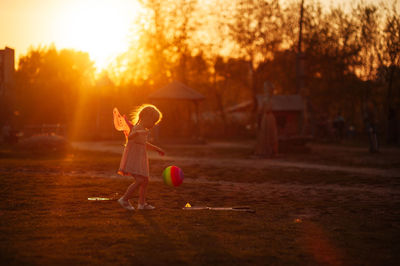 A girl in butterfly krulya plays with a ball on the field in the summer at the golden hour