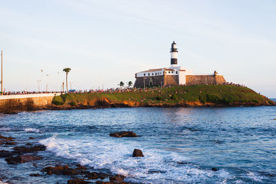 Lighthouse by sea against clear sky