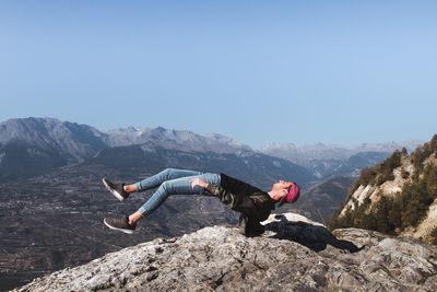 People on rock by mountains against clear sky