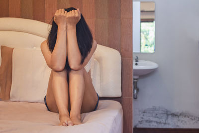 Worried woman sitting on bed at home