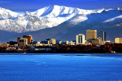 Scenic view of snowcapped mountains in front of buildings and river on sunny day