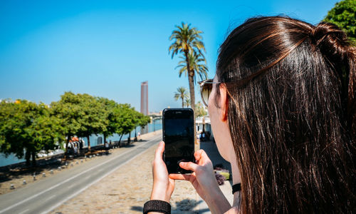 Man photographing with mobile phone against sky