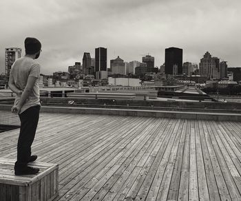 Rear view of man standing by river against cityscape