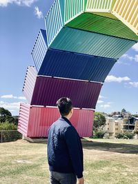 Rear view of man standing by building against sky