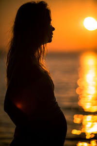 Woman standing by sea against sky during sunset