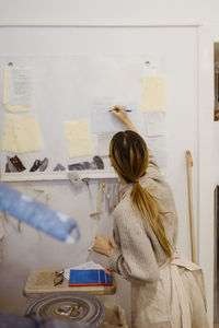 Female potter writing on paper while standing at workshop