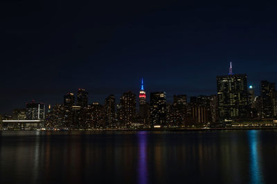 Illuminated buildings by river against sky at night