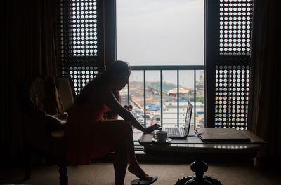 Woman working on laptop by door at home