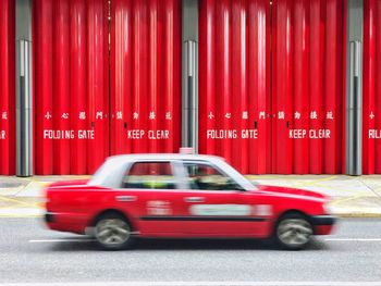 Blurred image of moving taxi against red metallic gate