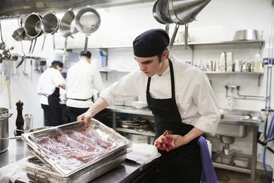 Male chef examining tray of meat wrapped with plastic in commercial kitchen