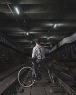 Rear view of young man with bicycle standing at railroad track