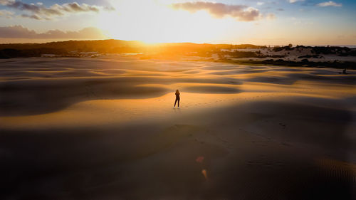 Rear view of man walking at beach against sky during sunset