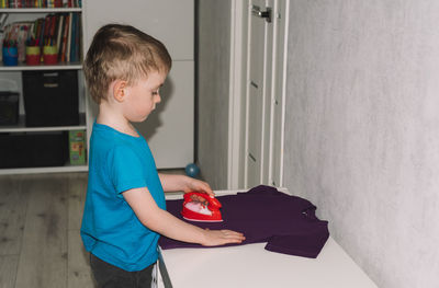 Boy ironing a t-shirt with a toy iron. housework, helper. child development concept