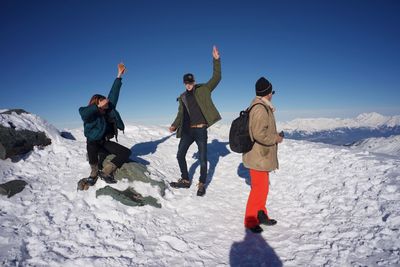 Friends enjoying on snow covered mountain against clear sky