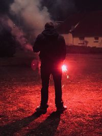 Rear view of man holding sparkler while standing on field at night