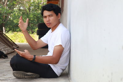 Side view of young man using mobile phone while sitting on wall