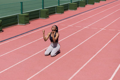 Cheerful black woman wins after running long distance on terracotta track of modern sports complex
