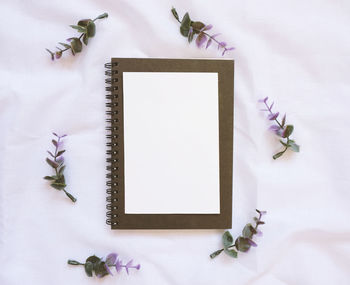 Directly above shot of spiral notebook with artificial flowers on fabric