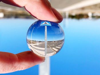 Close-up of hand holding crystal ball against blue sky