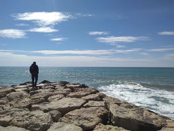 Man standing on rock by sea against sky