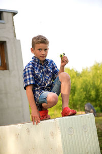 Portrait of boy crouching on retaining wall in yard