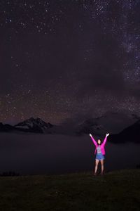 Rear view of woman doing yoga on field against sky at night