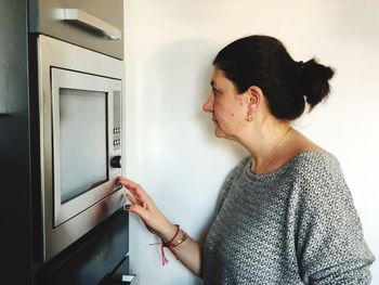 Side view of mature woman standing by microwave at home