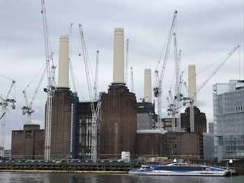 Cranes on harbor in city against sky