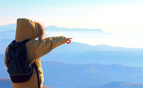 Rear view of teenage boy standing on mountain against sky