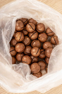 Top view of unpeeled macadamia nuts in a plastic bag on a wooden table.