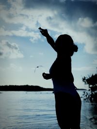 Silhouette woman standing in sea against sky