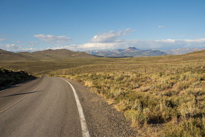 Country road amidst landscape against sky