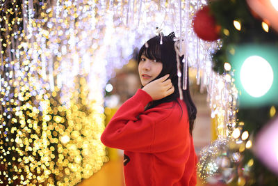 Portrait of young woman standing against christmas tree