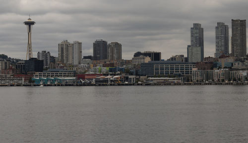 Buildings in city at waterfront against cloudy sky