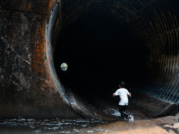 Rear view of a boy walking through a drainage tunnel