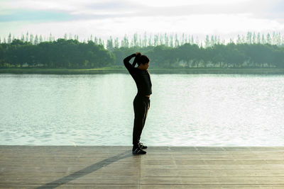 Side view of woman standing by lake against sky