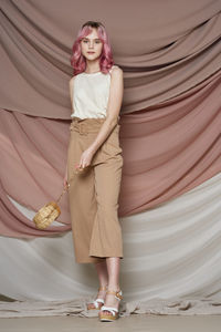 Full length portrait of young woman standing against curtain