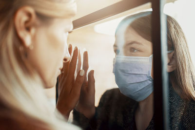 Close-up of mother and daughter looking at each other through window