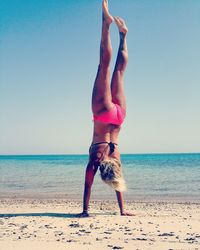 Rear view of woman in bikini practicing handstand at beach