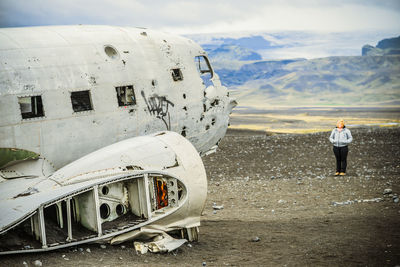 Full length of woman standing by abandoned airplane on sand