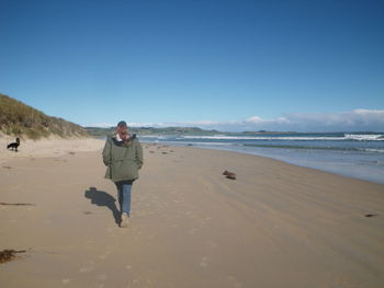 Full length of woman walking on beach against clear sky