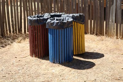 High angle view of trash cans against wooden fence on sunny day