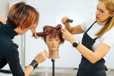 Hairstylist school - female adult student practicing how to make hair styling with hair roller