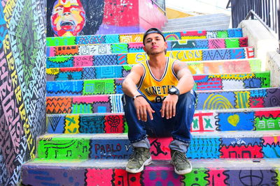 Portrait of young man sitting on multi colored graffiti