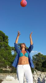 Mature woman playing with ball against clear blue sky