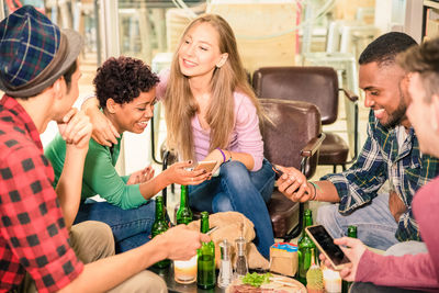 Smiling friends using phones while sitting in restaurant